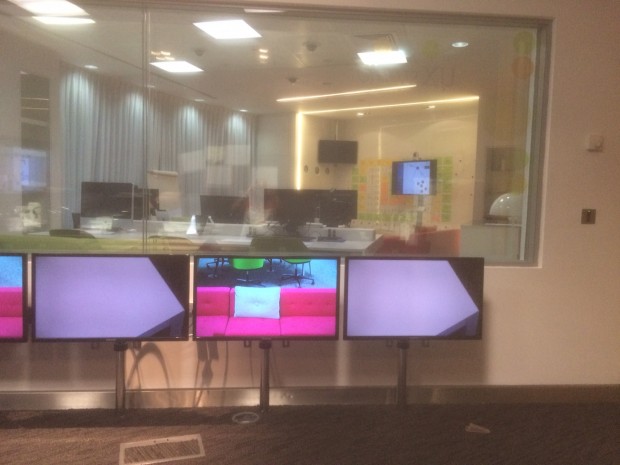 3 monitors on stands in front of a window. overlooking an office with monitors and keyboards