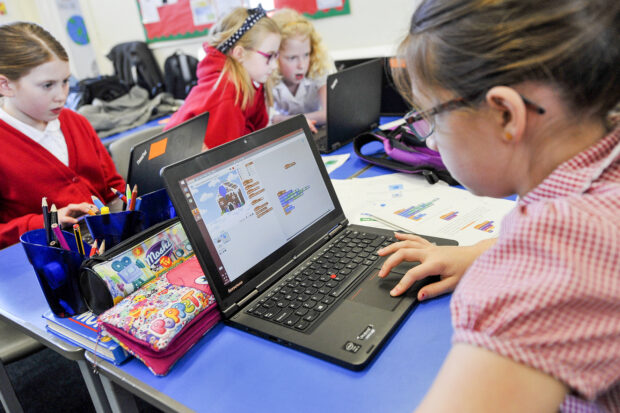 4 schoolgirls sitting at a desk working on laptops