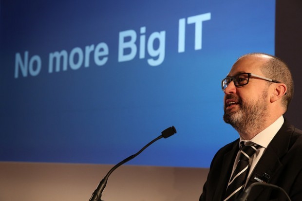 Mike Bracken standing in front of a microphone with a presentation on a the big sreen behind him 