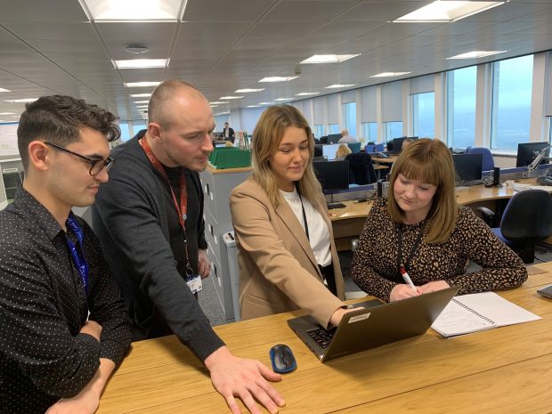 A group of people standing looking at a laptop