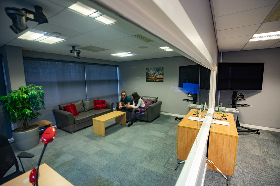 Reflection in a one way mirror in the DVLA UX lab of a man and a woman talking.