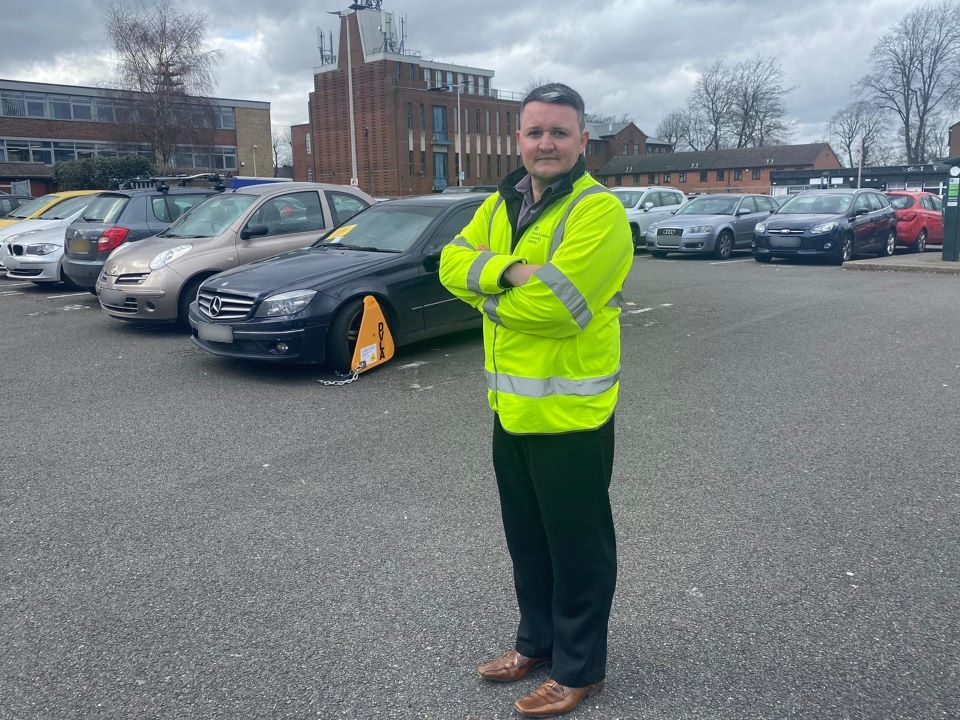 Paul Davies standing in front of a clamped vehicle in a car park.