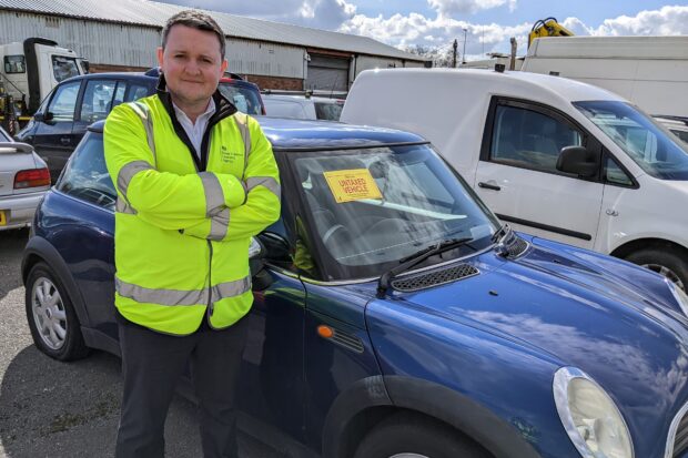 A man in a high-vis jacket standing next to an impounded MINI.